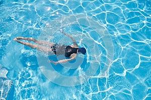 Young woman swimming underwater in an outdoor pool, top view of back of girl