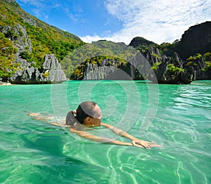 Young woman swims in the crystal clear water near of islands