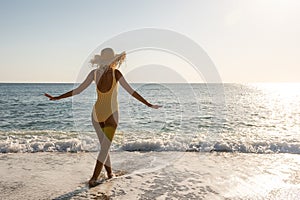 Young woman in swimsuit with hands apart on a sand beach. Summer holiday concept