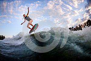 Young woman in swimsuit jumping up on surf style wakeboard against blue cloudy sky
