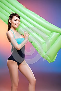 Young woman in swimsuit posing with swimming mattress and smiling at camera