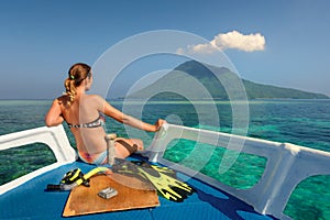 Young woman in swimsuit sit on boat looking to a island