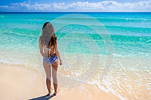 Young woman in a swimsuit standing on the beach and looking at t
