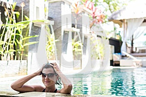 Young woman in swimsuit in swimming pool in gorgeous resort, luxury villa, tropical Bali island, Indonesia.