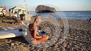 young woman in swimsuit, uses laptop, sitting on pebbles beach by the sea, hot summer day. Close-up shot of happy