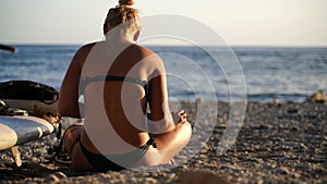 young woman in swimsuit, uses laptop, sitting on pebbles beach by the sea, hot summer day. Close-up shot of happy