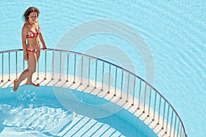 Young woman in swimsuit walks on ledge separating pools