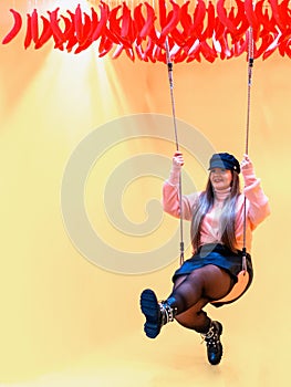 Young woman on swing with yellow background
