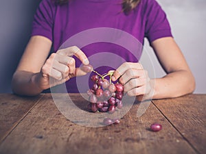 Young woman at table eating grapes