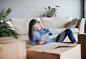 A young woman with tablet and cardboard boxes moving in a new home.