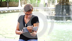 Young woman with tablet computer sitting in city park