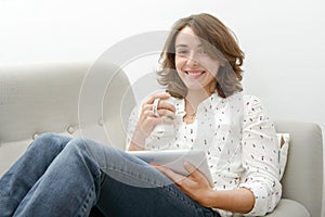 Young woman with a tablet drinks a cup of tea