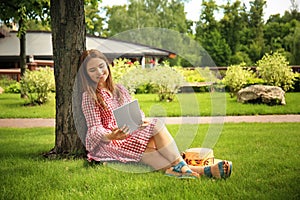 Young woman with tablet PC sitting near tree in park