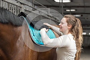 Young woman tacking up her Hanoverian horse in a stable in Brilon, Germany photo