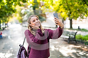 Young woman take selfie from hands with phone on summer city street. Urban life concept