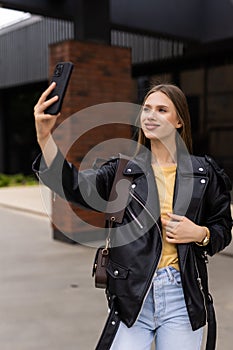 Young woman take selfie from hands with phone on summer city street. Urban life concept