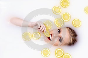 Young woman takes a bath with milk and citrus fruits. Woman eats a lemon