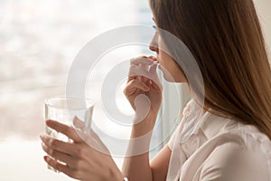 Young woman takes pill with glass of water in hand