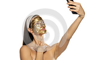 Young woman takes selfies with golden mask on her face