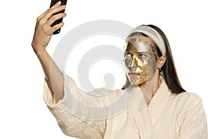 Young woman takes selfies with golden mask on her face