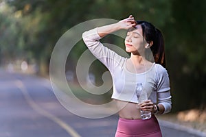 A young woman takes a short break and drinks water during exercising in a public park