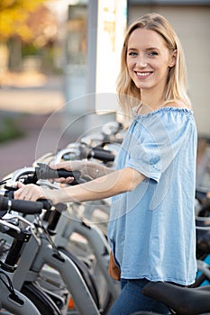 Young woman taking bike from row rental bicycles