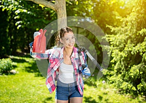 Young woman taking break from gardening holding up watering can and shears