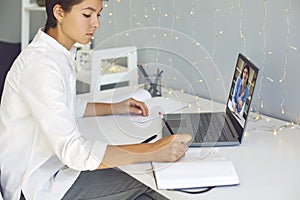 Young woman taking notes during online consultation with coach or video lesson with teacher