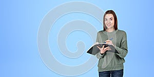 Young woman taking notes and smiling, copy space blue background