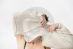 Young woman is taking off her sweater, covering her face.