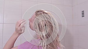 Young woman taking off a towel from her head and shaking her wet hair in bathroom