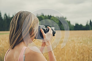 Young woman taking photo of beautiful wheat field