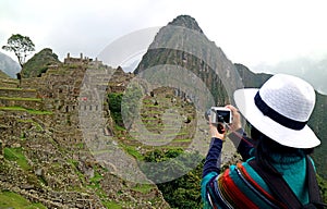 Young woman taking picture of the Inca ruins in Machu Picchu, UNESCO world heritage site in Cusco region of Peru