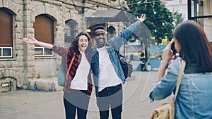 Young woman is taking pictures of beautiful couple African American guy and Caucasian girl standing in the street and