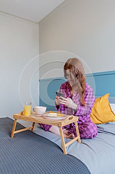 Young woman taking pictures of her breakfast while sitting in bed