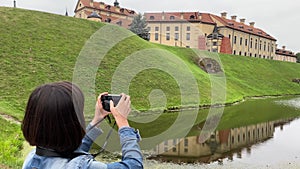 Young woman taking pictures on her camera while traveling in Europe. Tourist in casual cloths taking photo of an old castle