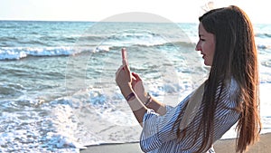 Young woman taking pictures of the sea on the phone