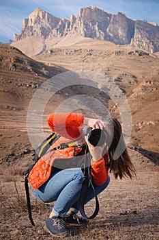 young woman taking pictures while sitting on the background of mountains