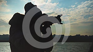 Young woman taking pictures of the sunset on the background of the sea, city and sky.