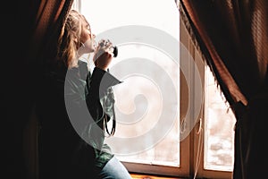 Young woman taking pictures through window while sitting on windowsill