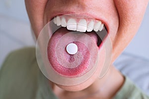 Young woman taking pill. Closeup of white round pill on tongue. Open mouth holding tablet