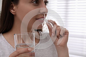 Young woman taking pill indoors, closeup