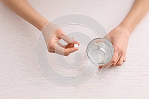 Young woman taking pill at table, top view