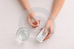 Young woman taking pill at table, top view
