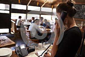 Young woman taking a reservation by phone at a restaurant photo
