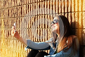 Young woman taking selfie in front of a brick wall