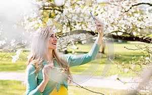 Young woman taking selfie with her phone in park at tree blossom
