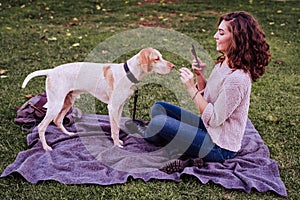 young woman taking a selfie with mobile phone with her dog at the park. autumn season