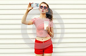 Young woman taking selfie picture by smartphone with coffee cup blowing red lips sending sweet air kiss wearing red heart shaped