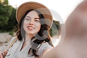Young woman taking selfie portrait outside. Smiling happy girl wearing hat enjoying summer holidays at the beach